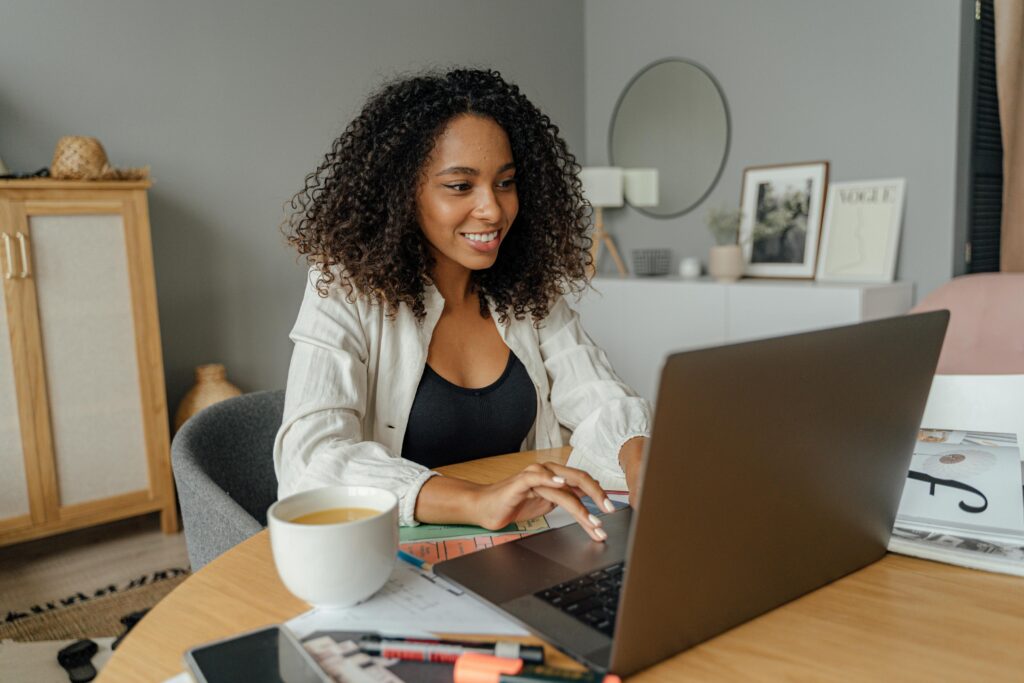 pexels-photo-5244025-5244025 A woman sits at a round table, working on a laptop with a coffee cup nearby in a cozy home office setting.